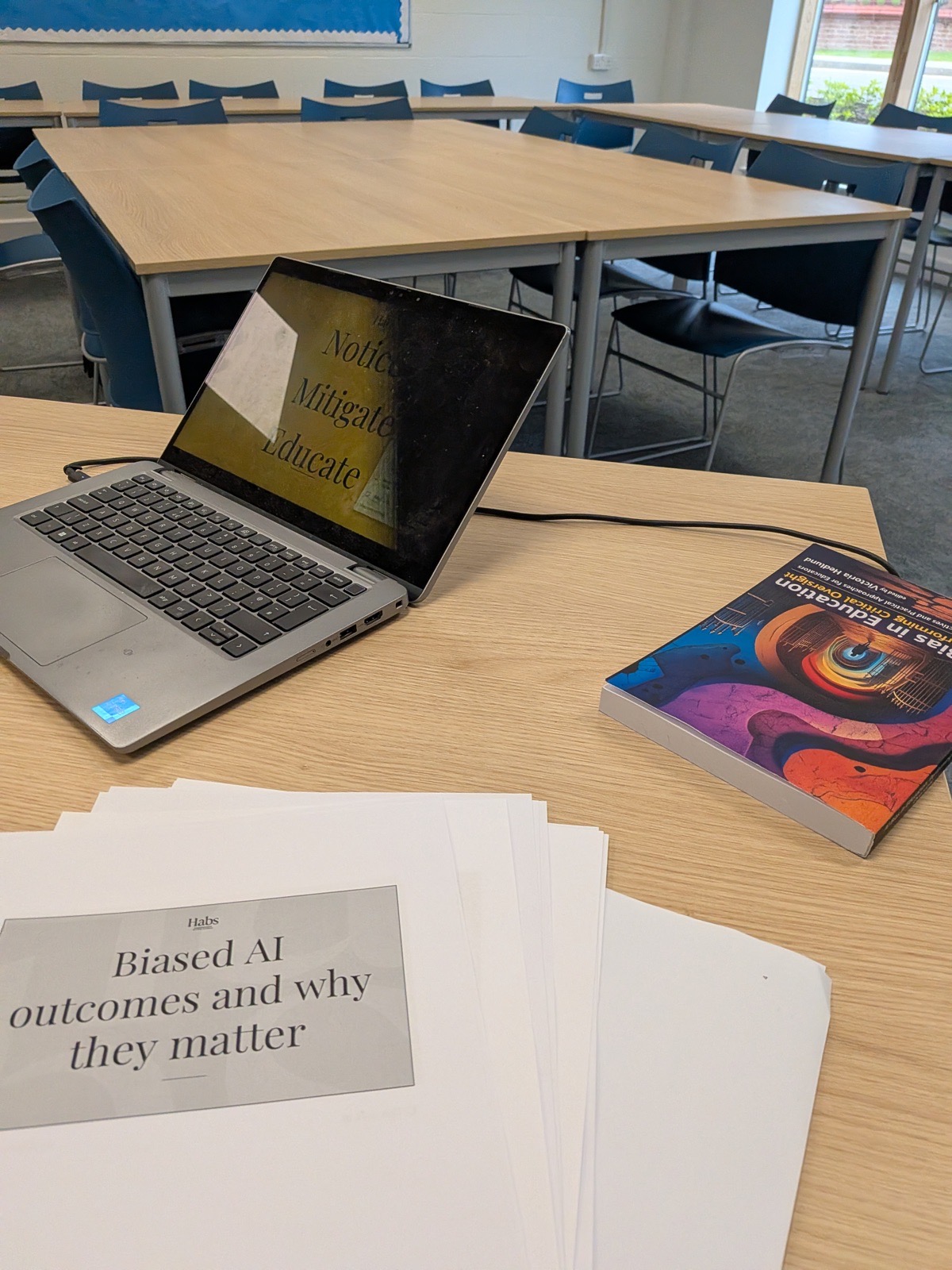 Laptop displaying the 'Notice, Mitigate, Educate' slide, alongside printed title slides and the book Biases in Education, set up ahead of the panel