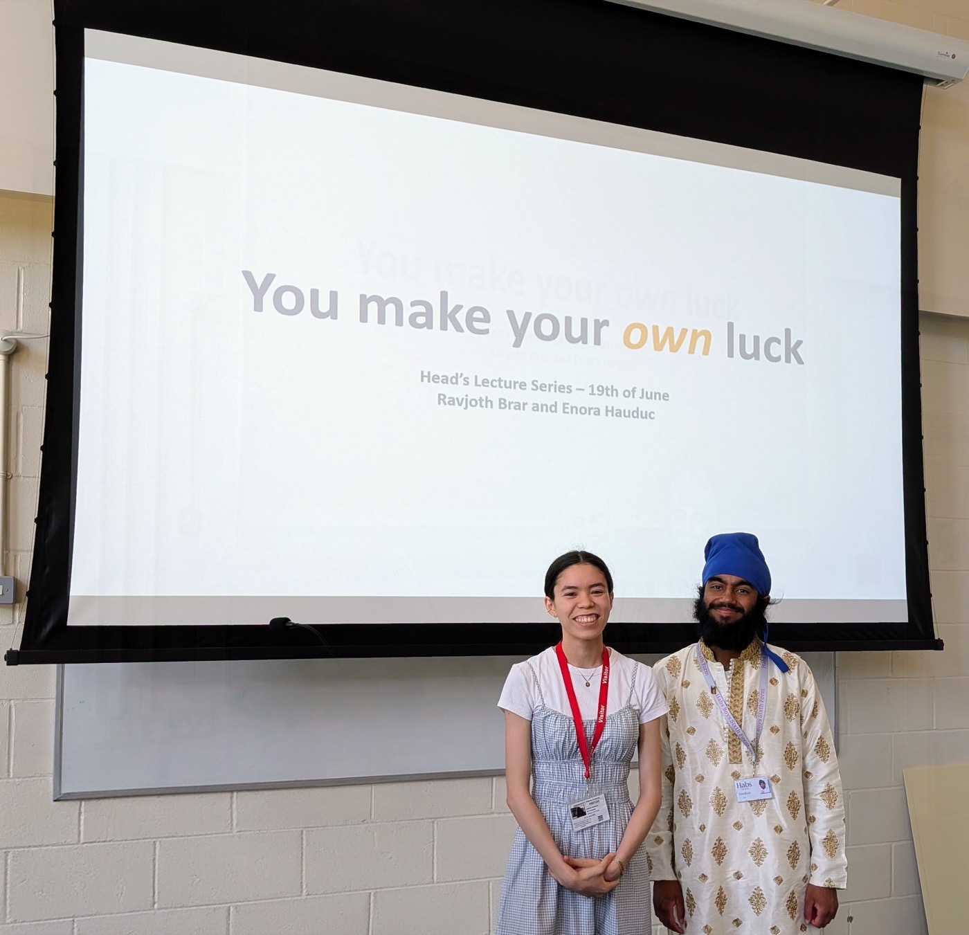 Ravjoth Brar and Enora Hauduc standing in front of the title slide for 'You make your own luck' at the Heads' Lecture Series